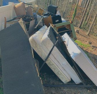 A pile of mattresses , chairs , and other furniture is sitting on the ground.