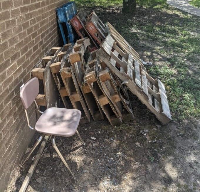 A chair sits next to a pile of wooden pallets