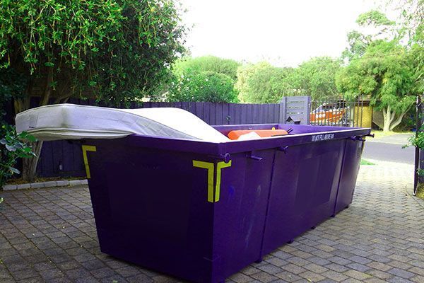 A large purple dumpster is sitting on a brick driveway.