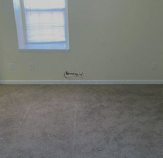 An empty room with a window and a carpeted floor.
