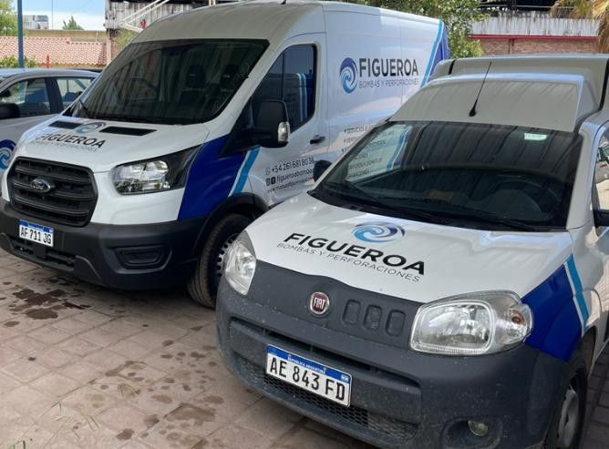 Dos furgonetas de servicio blancas y azules con la inscripción "FIGUEROA" estaban estacionadas en un terreno pavimentado.