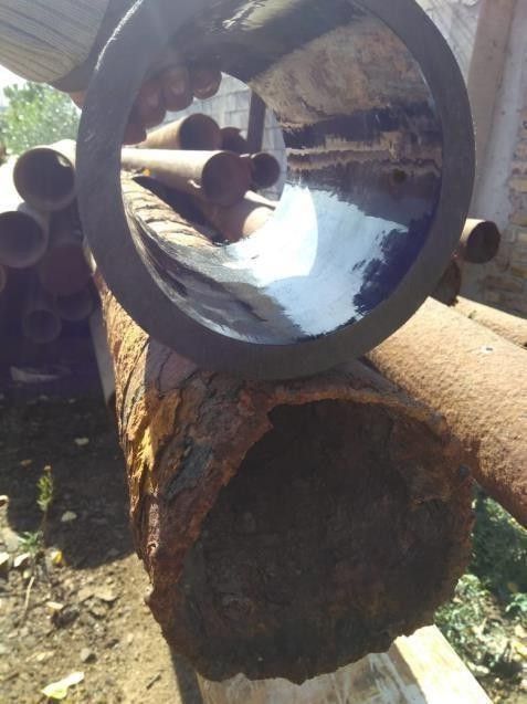 Una persona sostiene un tubo liso y limpio sobre un tubo de metal muy corroído y oxidado al aire libre.