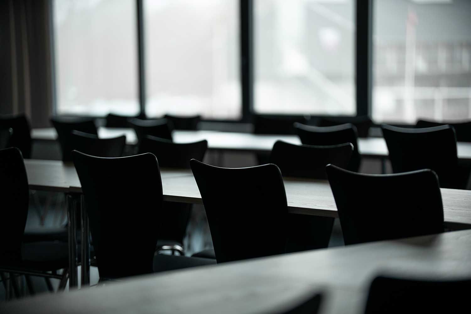 Tomt klasseværelse med rækker af stole og borde foran et vindue.