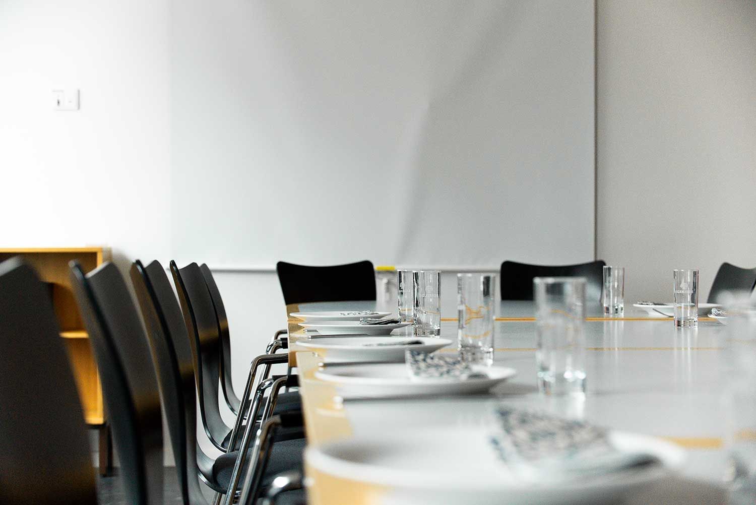 Mødelokale til konference med whiteboard, glas, tallerkener og stole.