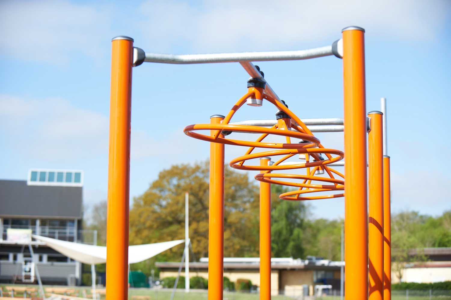En række orange stænger i en park med en bygning i baggrunden.