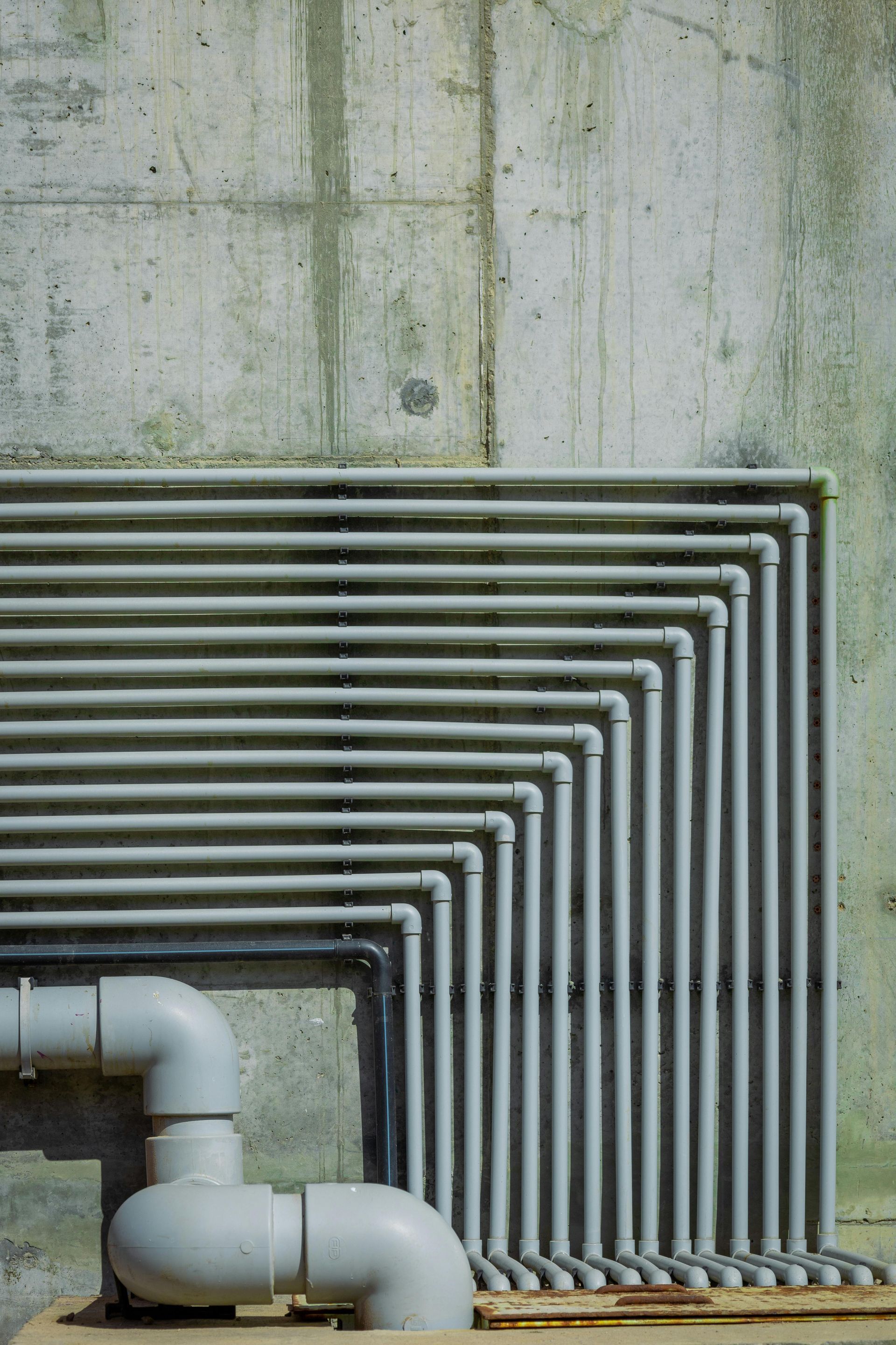 Gray metal pipes arranged in a neat right-angle pattern against a concrete wall