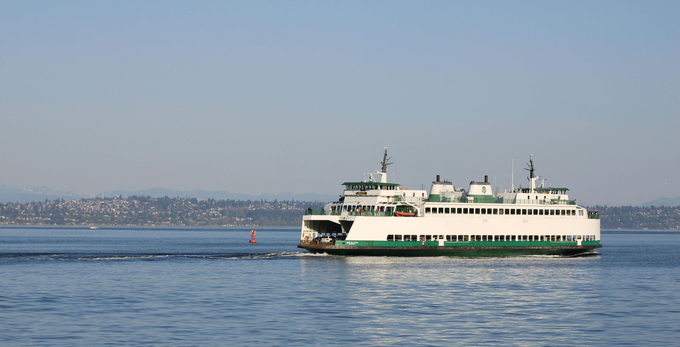 Large white and green ferry crossing calm blue water with a distant shoreline in the background