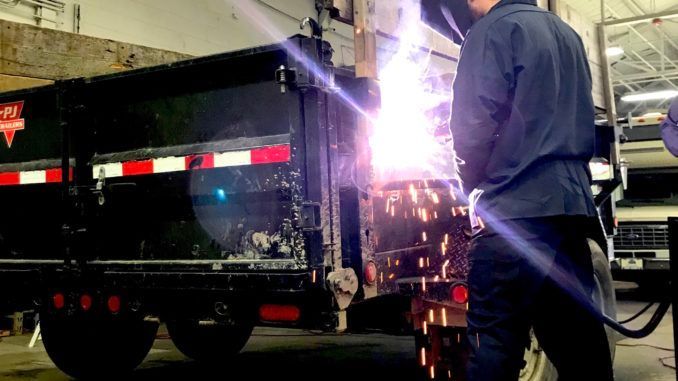 A man is welding a trailer in a garage.