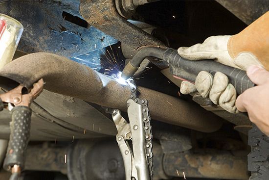 A person is welding a pipe under a car.