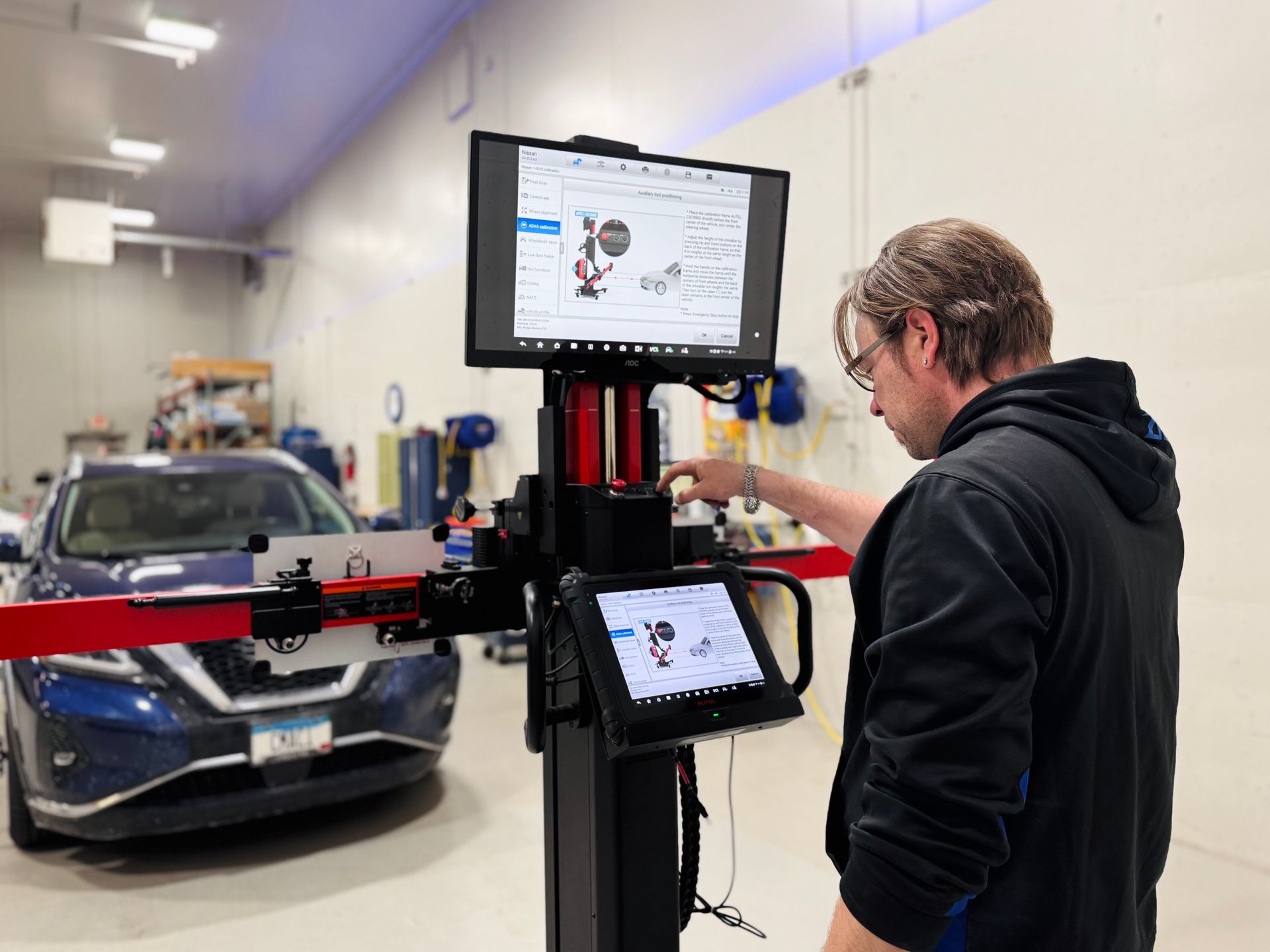 Mechanic uses alignment system on car in shop. A blue car is in the background.