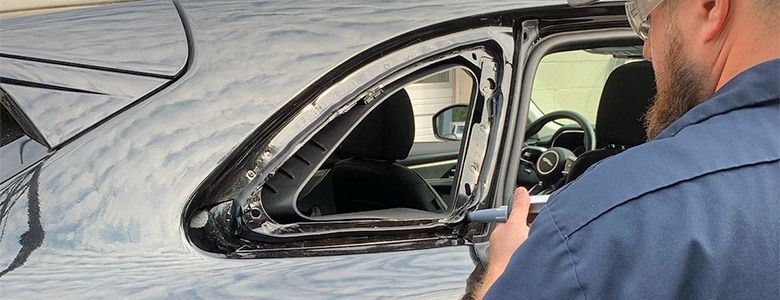 A person repairs a car window frame on a black vehicle.