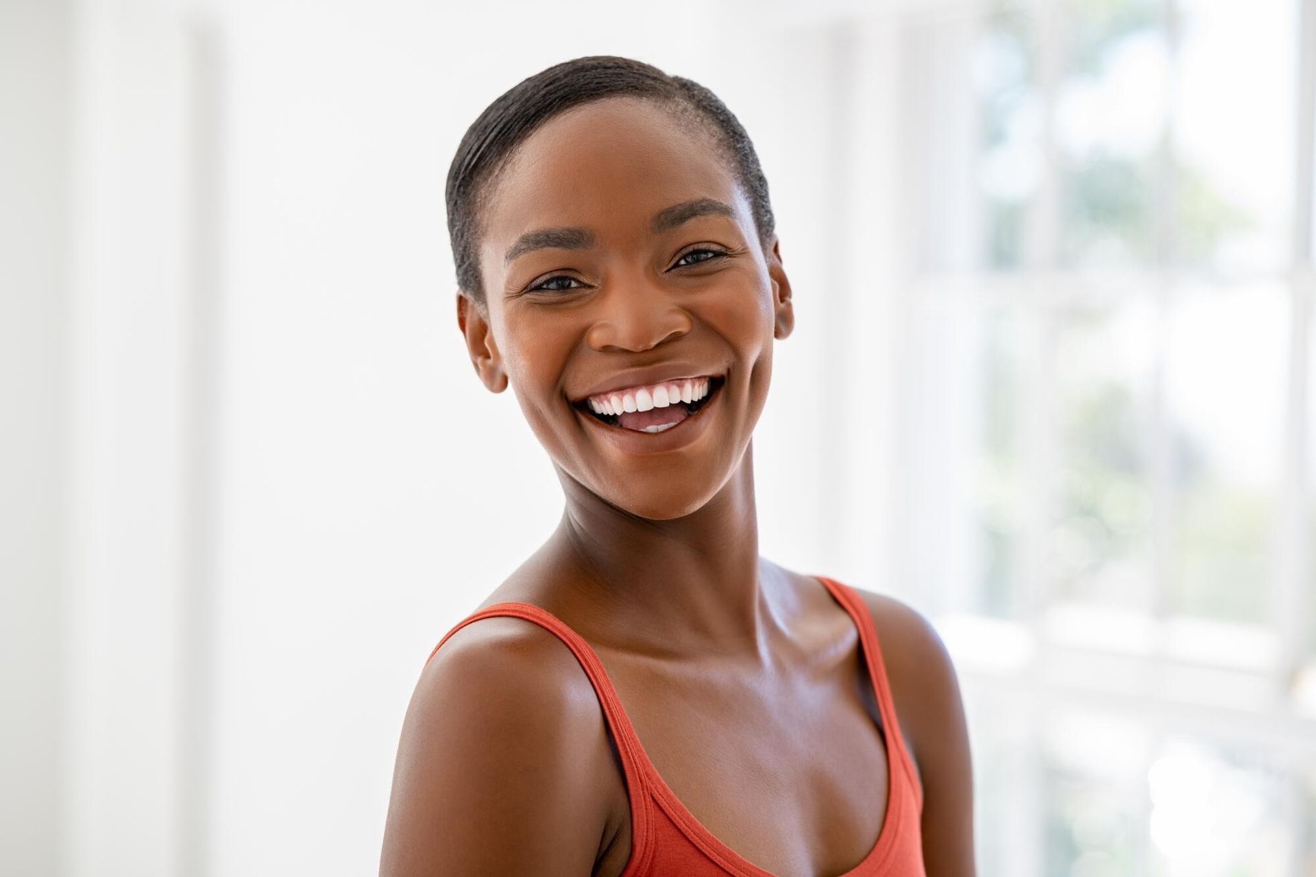 A woman in a red tank top is smiling and looking at the camera.