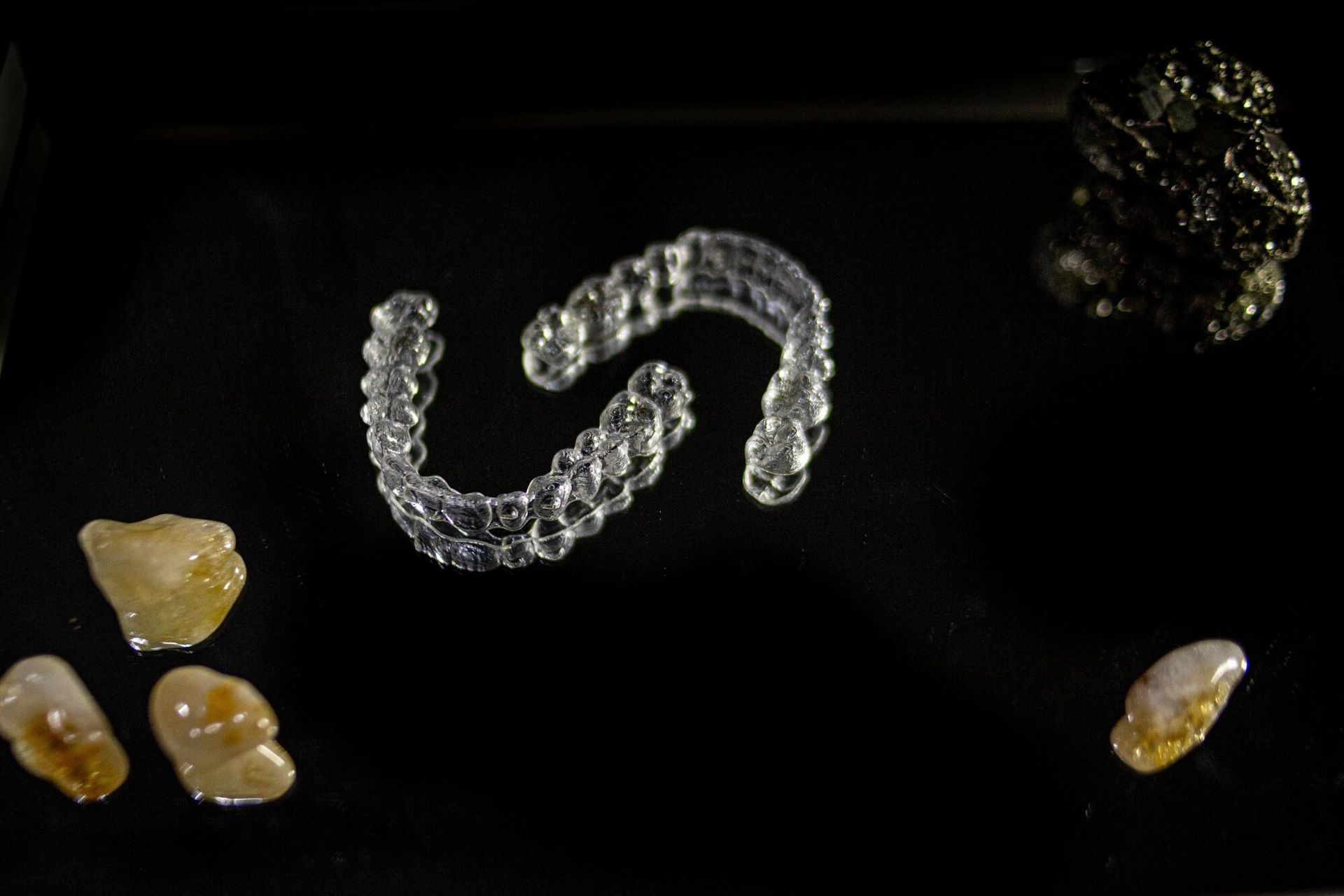 Clear dental aligners and several small, rough rocks arranged on a black surface.