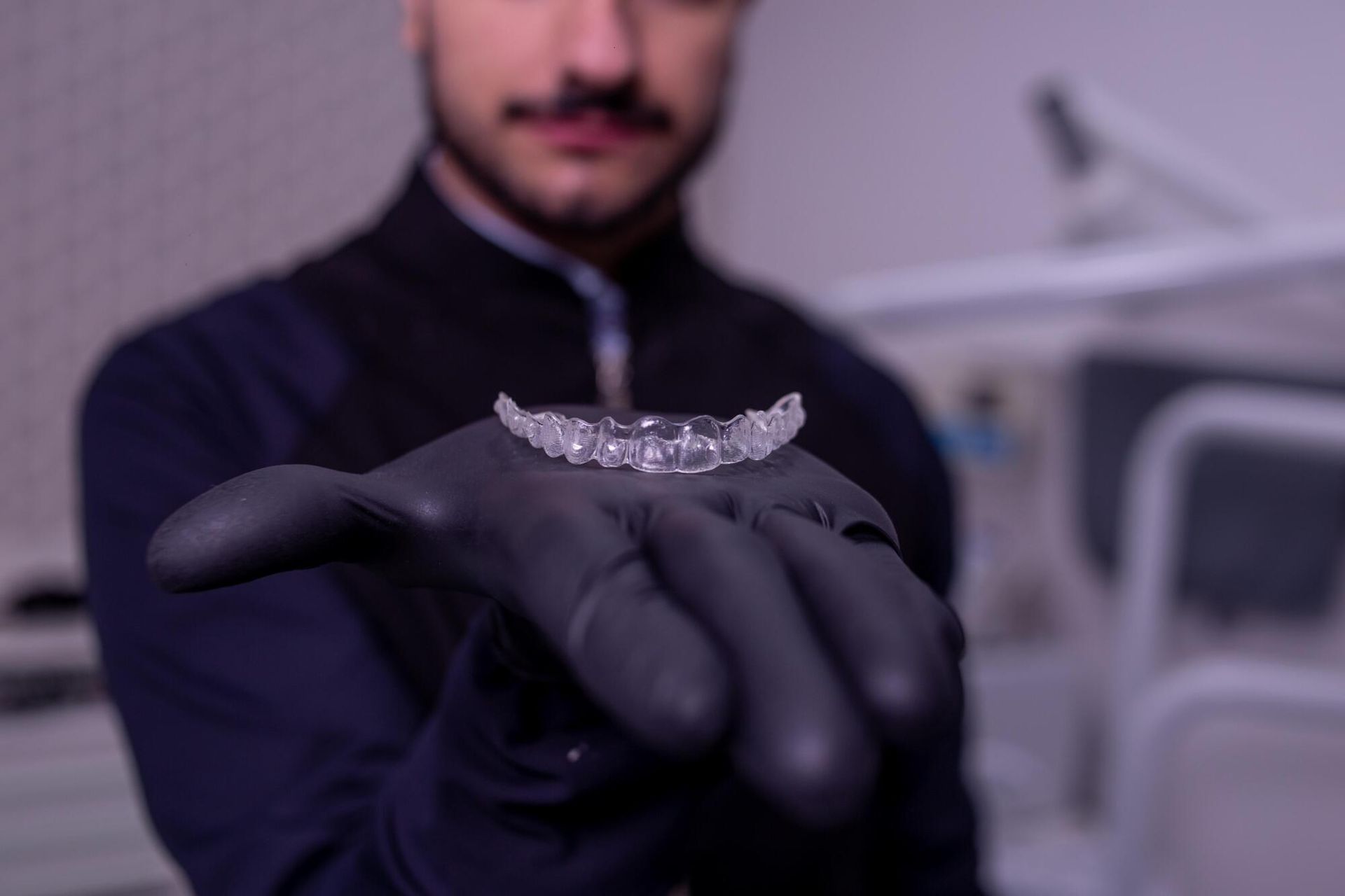 Man in black gloves holding clear aligner in a dental office.