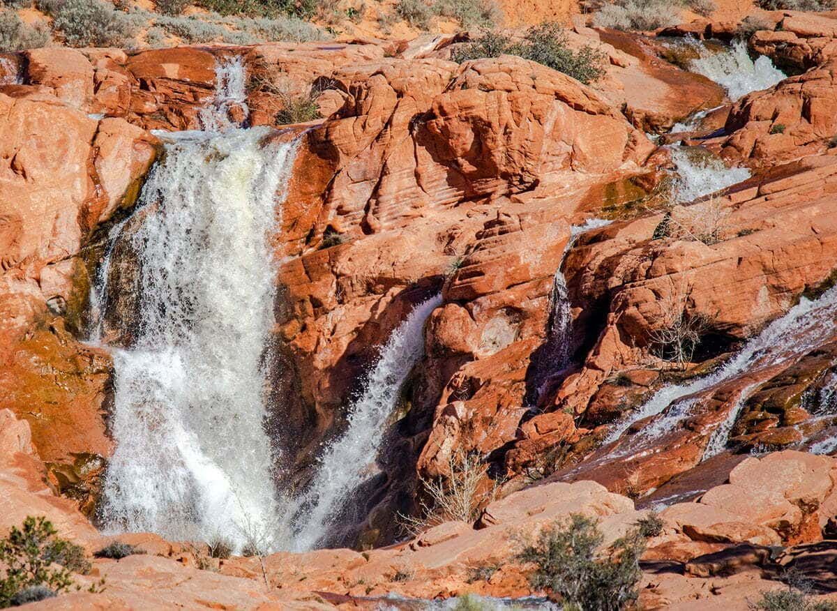 Waterfall cascading over red sandstone rocks in a desert landscape.