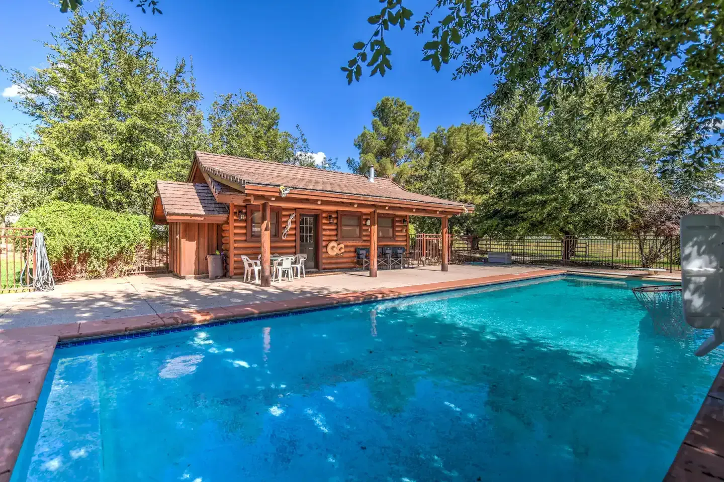 A rectangular pool reflects the red rock landscape near a rustic cabin under a blue sky.