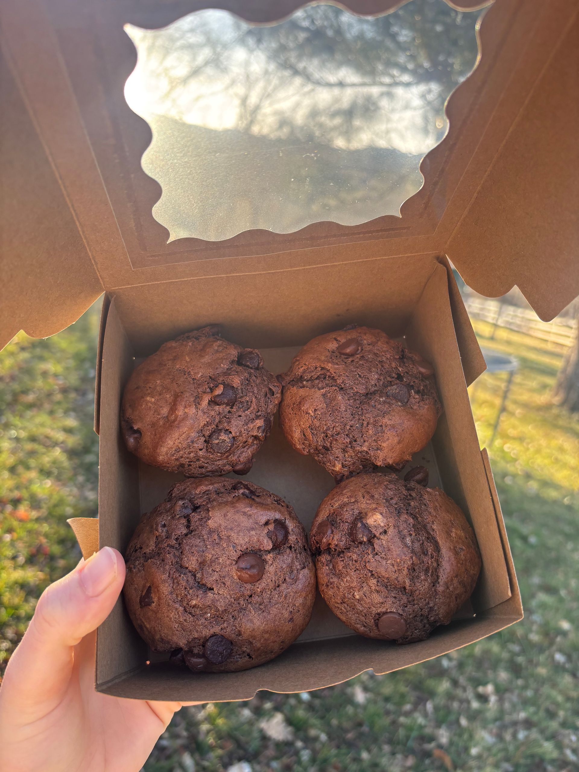 Display of artisanal breads, granola, honey jars, and pastries on a wooden table outdoors.