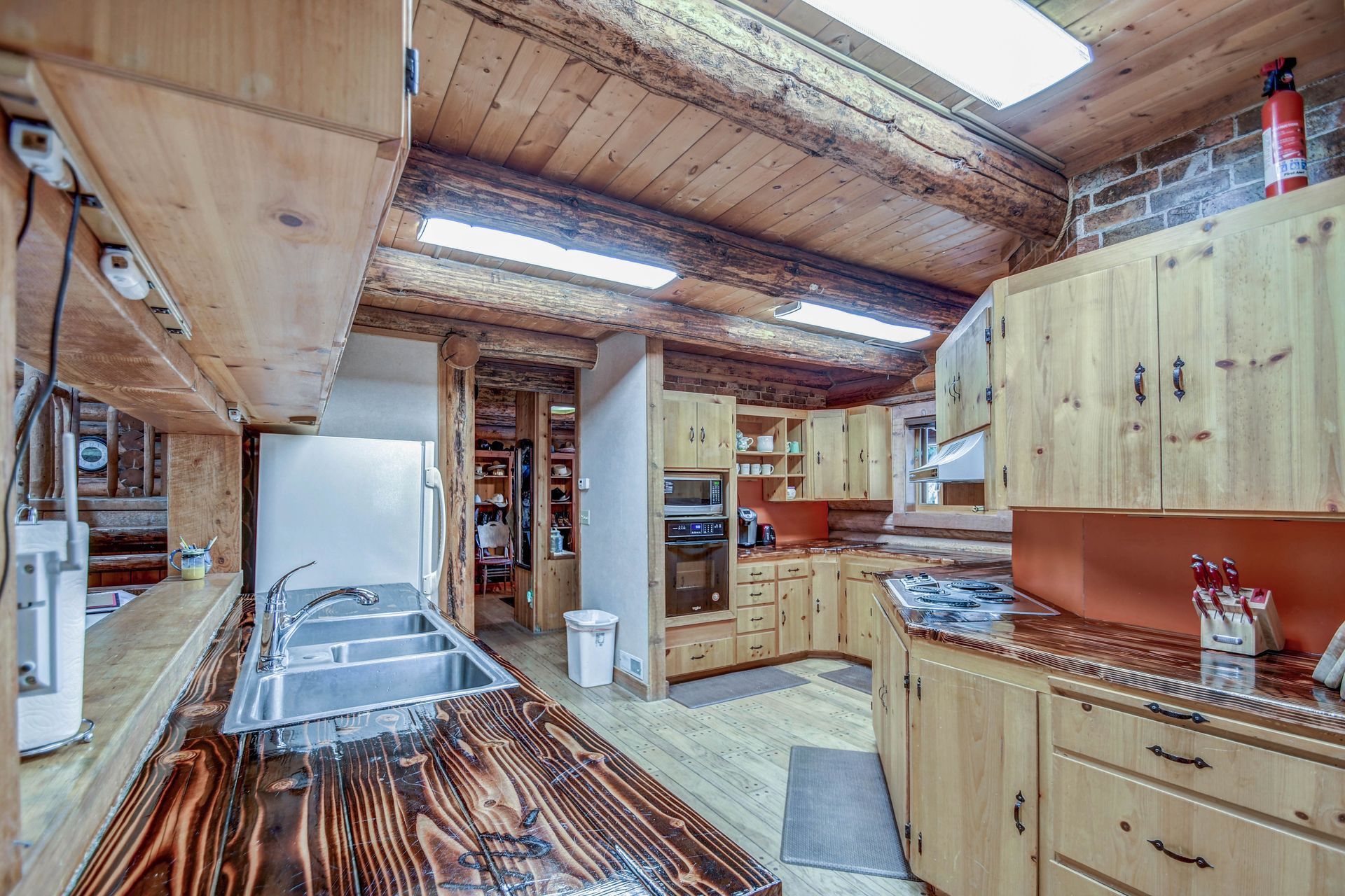 Rustic kitchen with wood cabinets, island, and ceiling beams, stainless steel appliances, and a window.
