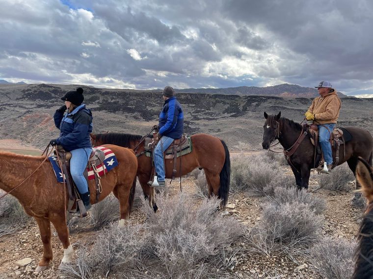 Three people on horseback in a barren landscape under a cloudy sky.