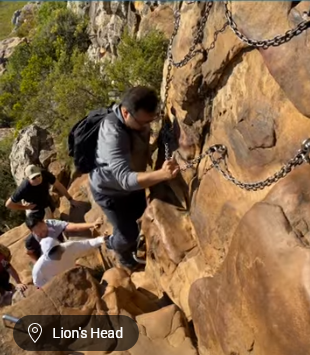 Hikers climbing a steep rock face with chains at Lion's Head trail