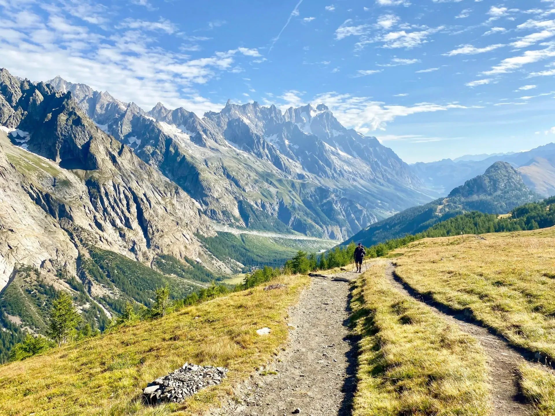A person is walking down a dirt path in the mountains.
