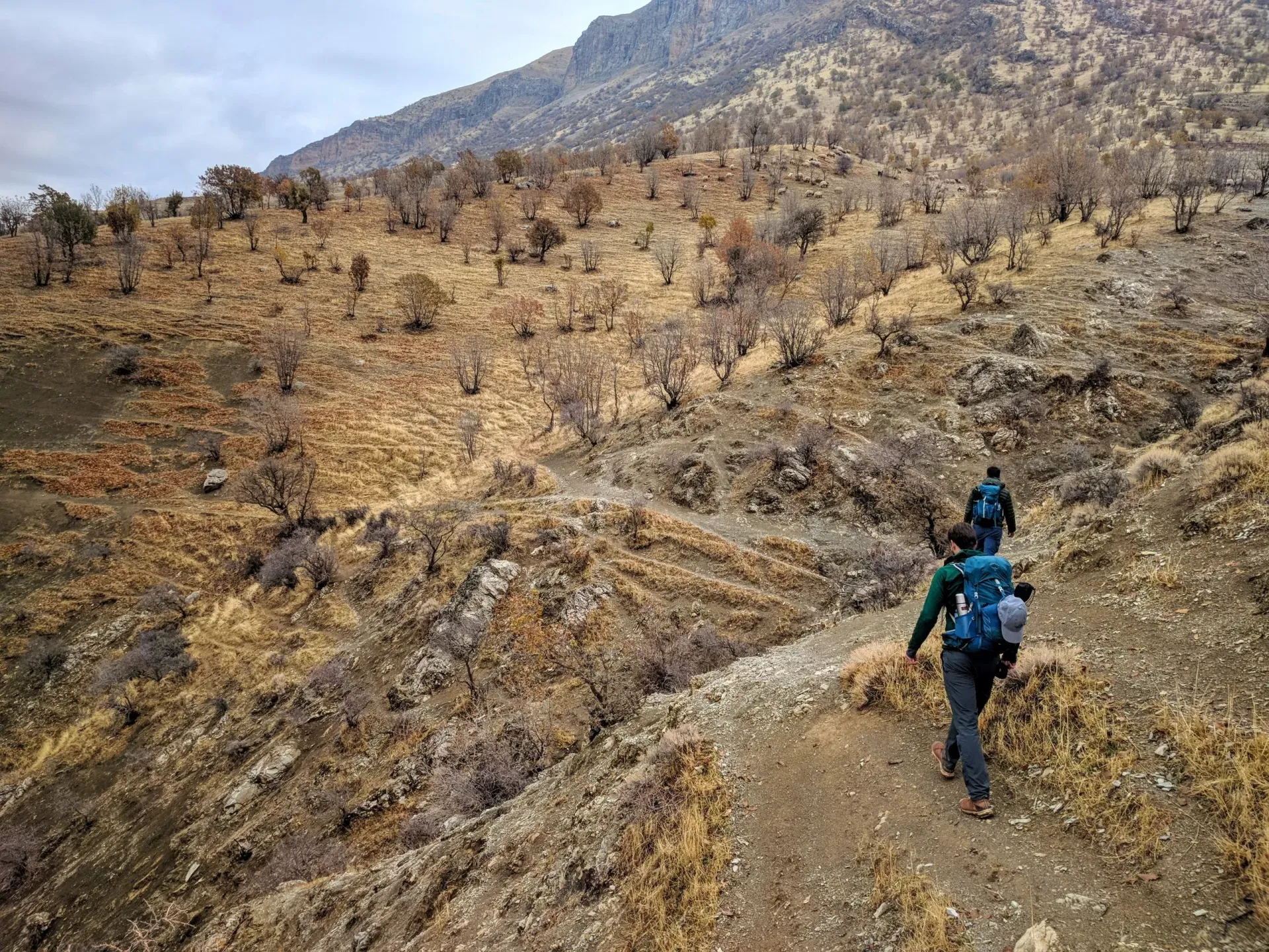 Two people are walking down a dirt path in the mountains.