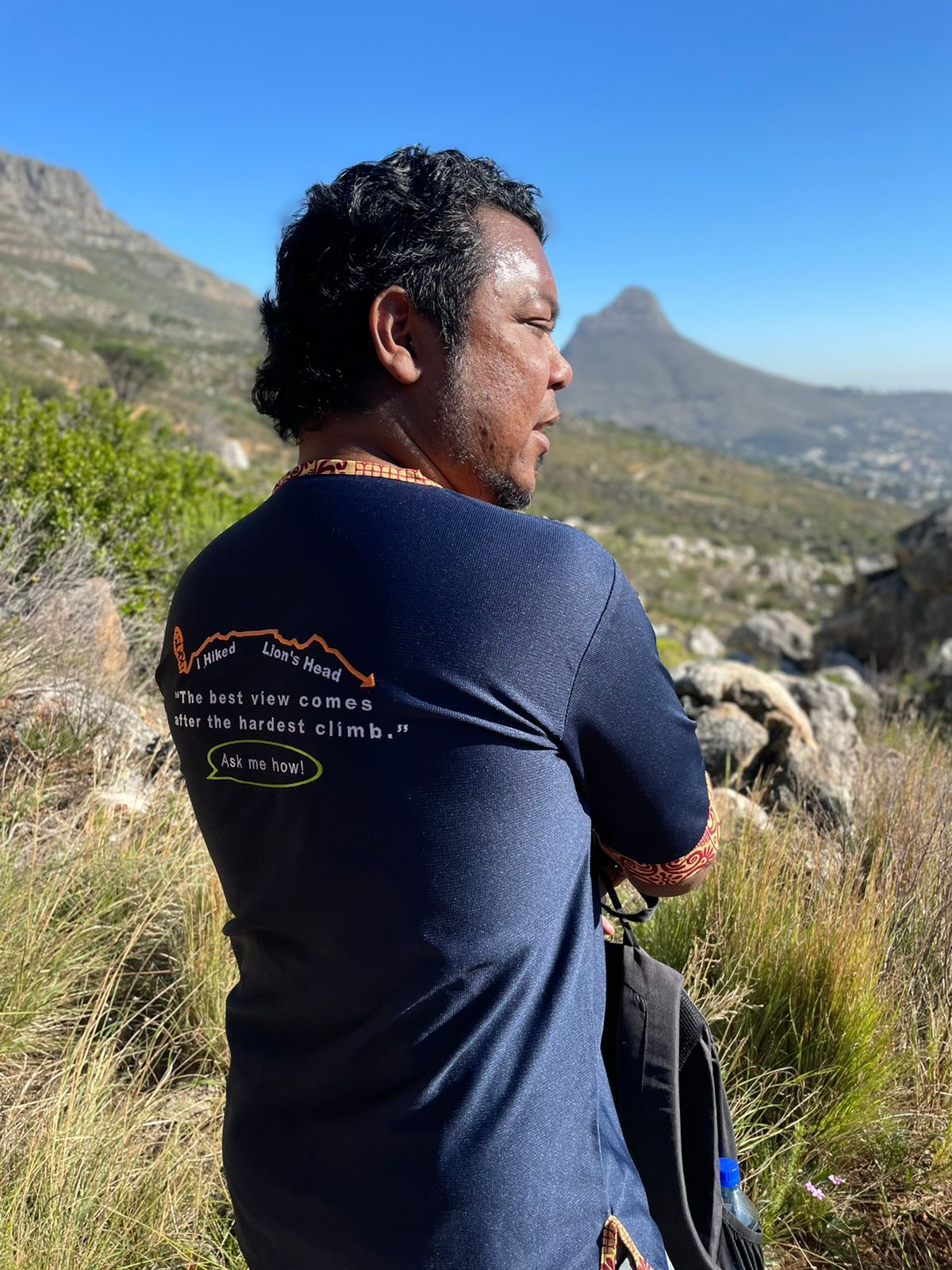 A man in a blue shirt is standing in a field looking at a mountain.