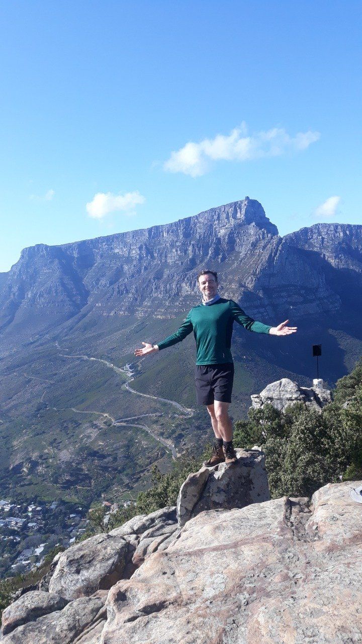 A man is standing on top of a mountain with his arms outstretched.