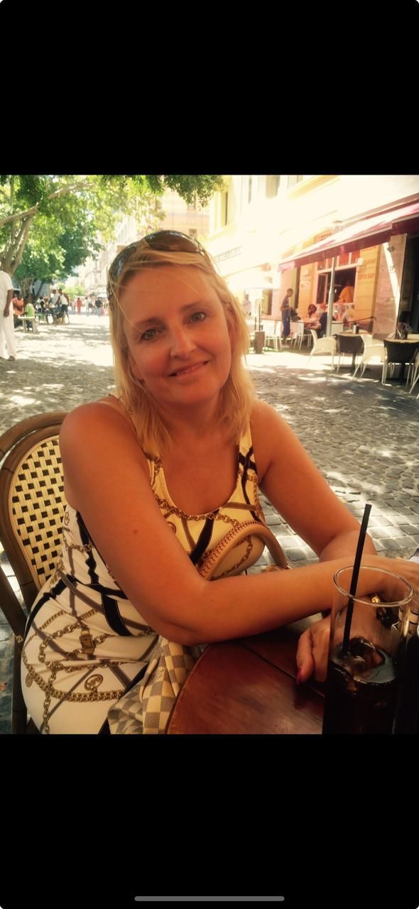 A woman is sitting at a table with a drink in her hand.