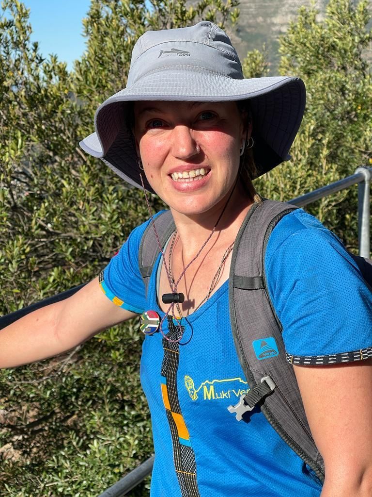 A woman wearing a hat and a backpack is smiling.