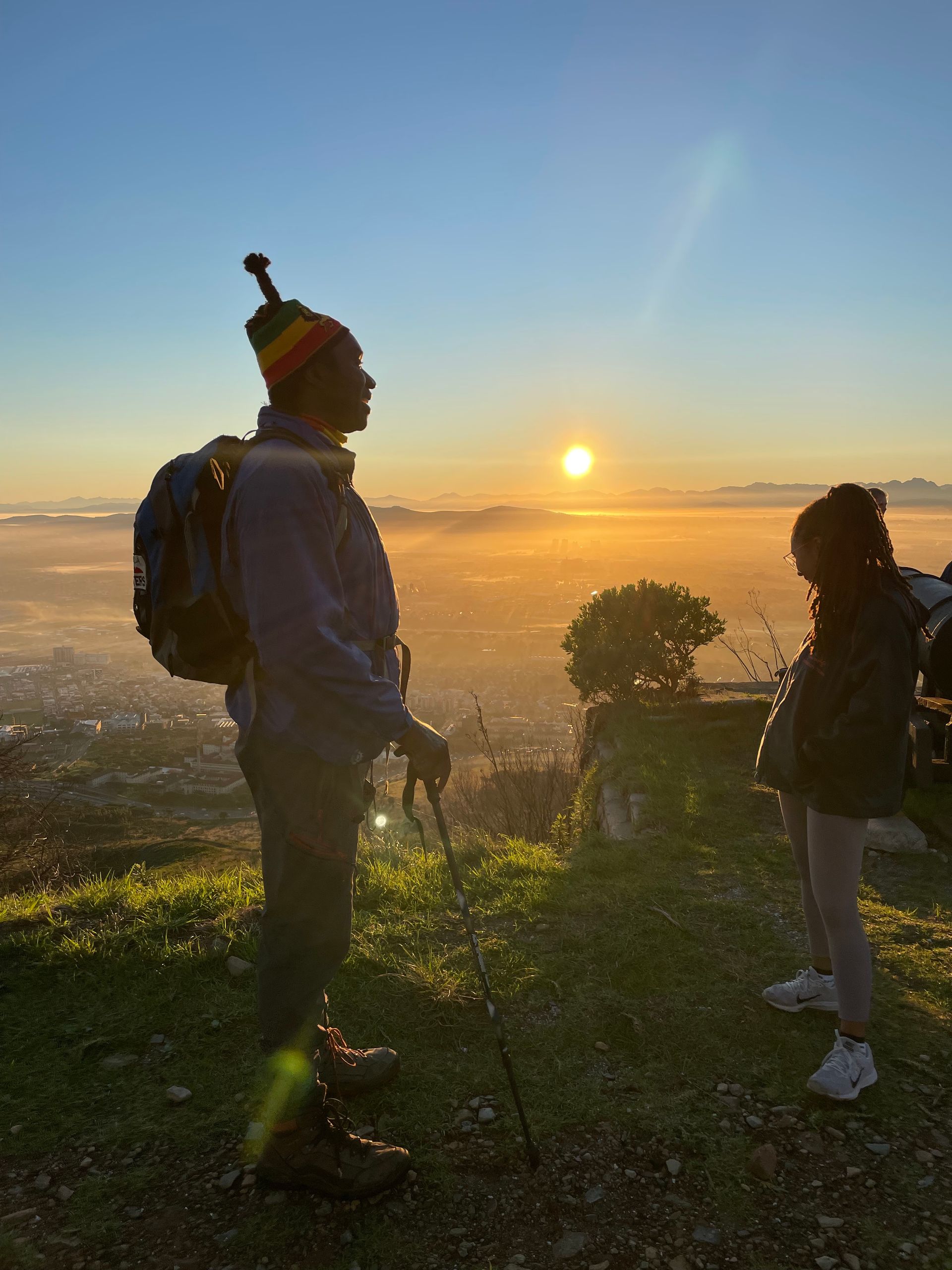 Two hikers silhouetted at sunrise on a grassy hill overlooking a foggy valley