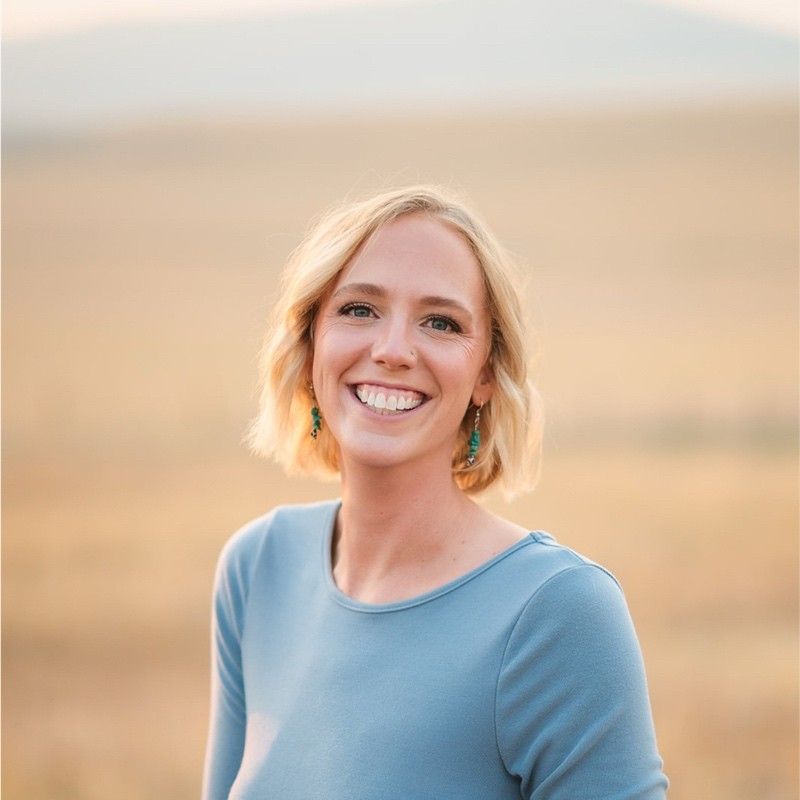 Woman with short blonde hair smiles in a field, wearing a blue top.