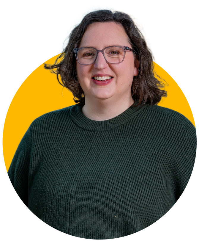 Woman with glasses smiling, wearing a dark green sweater, against a yellow background.