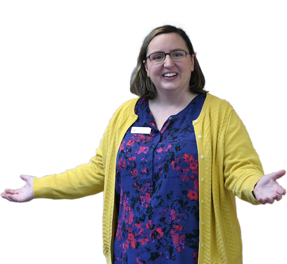 Woman with glasses smiles, arms outstretched, wearing a yellow cardigan over a blue floral top.
