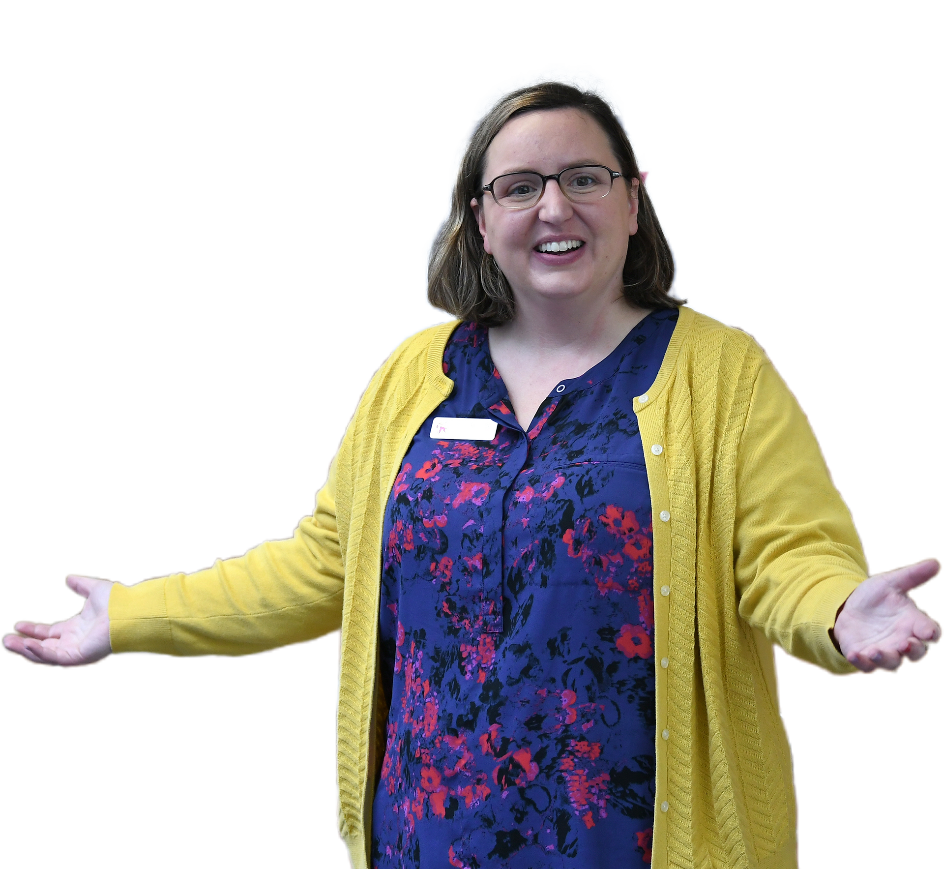 Woman with glasses smiles, arms outstretched, wearing a yellow cardigan over a blue floral top.