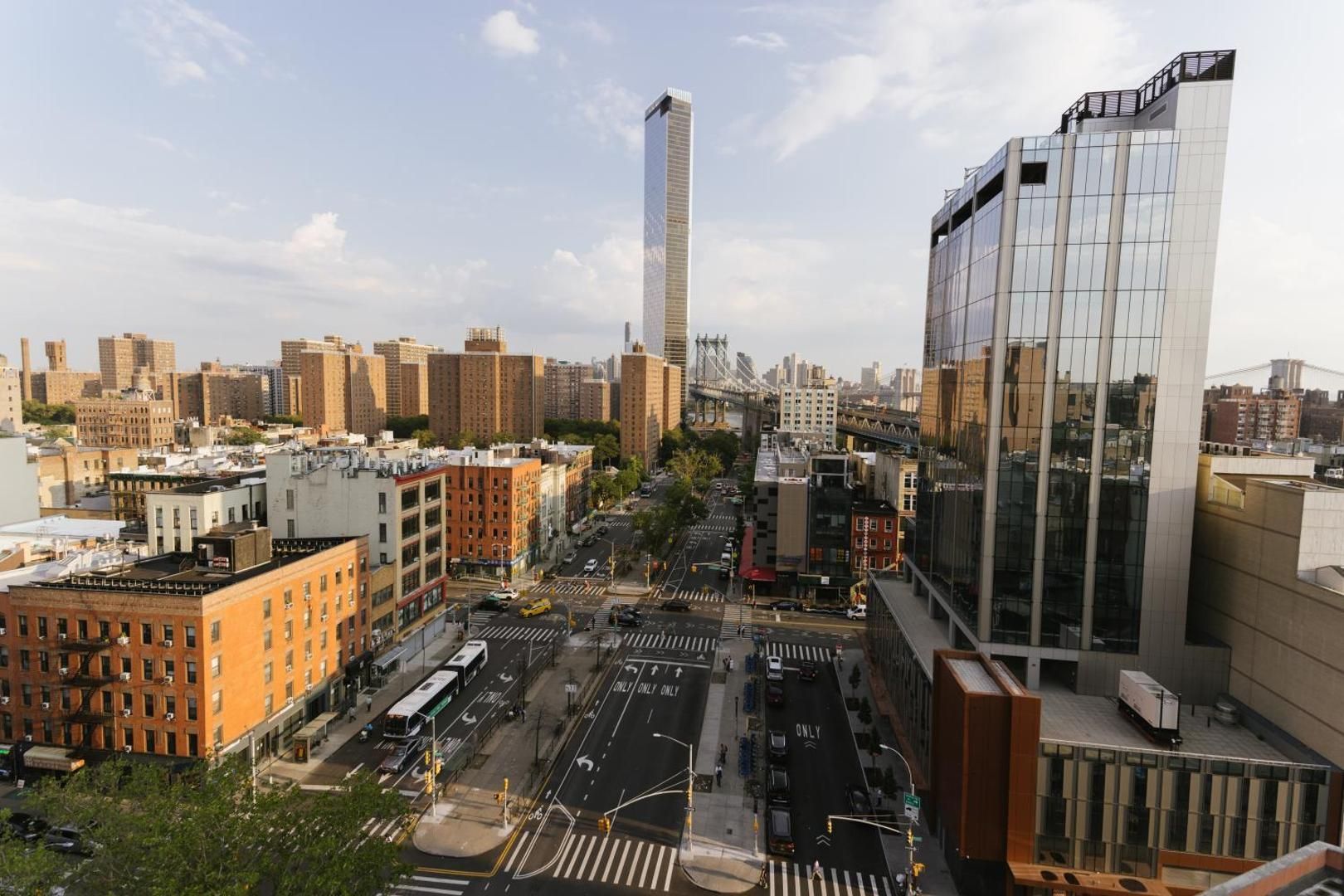 Cityscape: Midtown Manhattan buildings, busy street, tall glass skyscraper in the background under a cloudy sky.