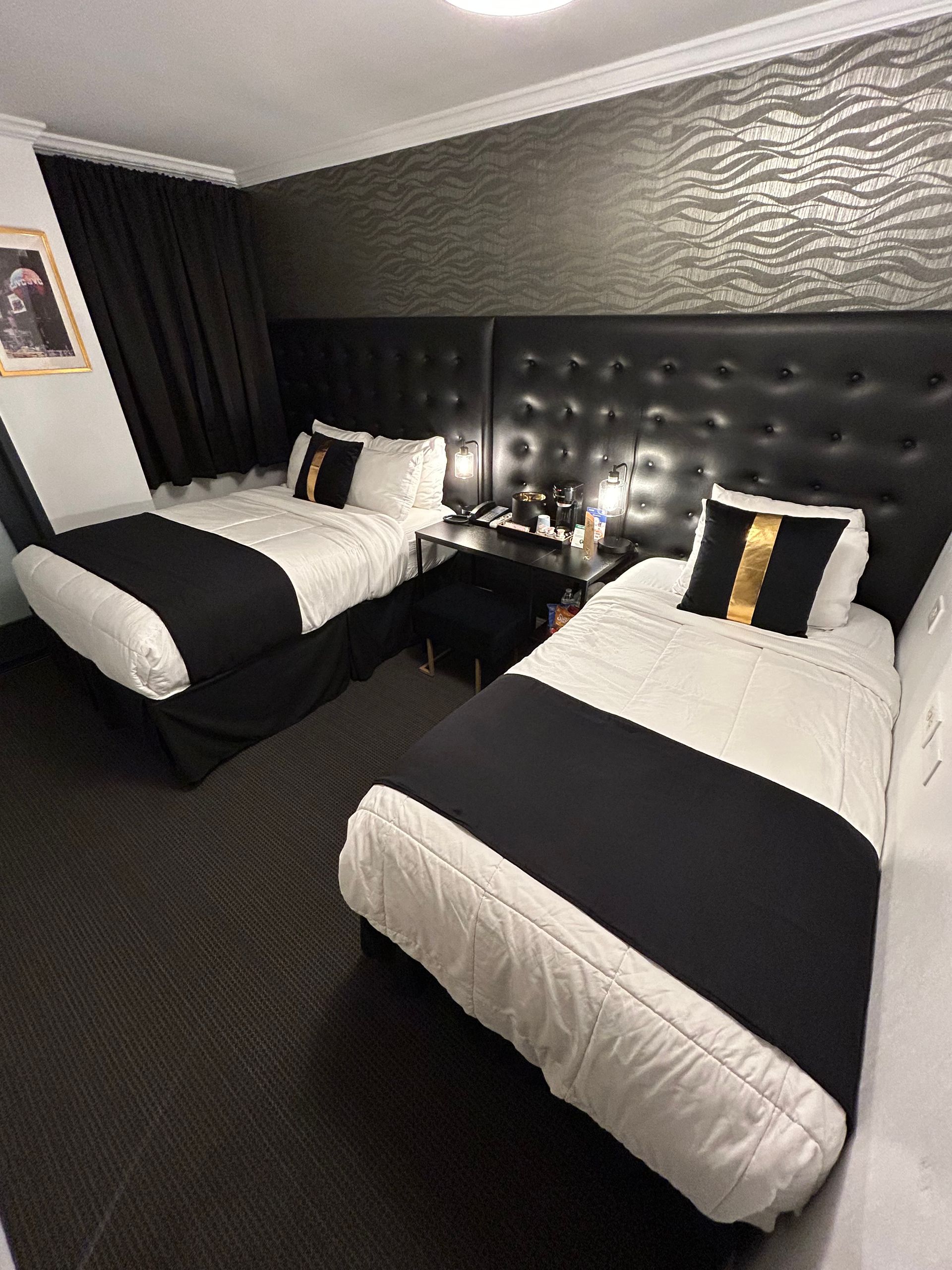 Two twin beds in a dark hotel room with black and white bedding, decorative headboard, and patterned wall.