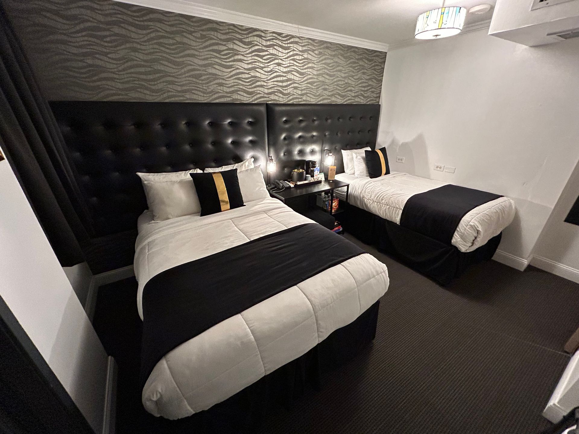 Two beds in a room, black and white bedding, black headboards, textured wallpaper, dark carpet.