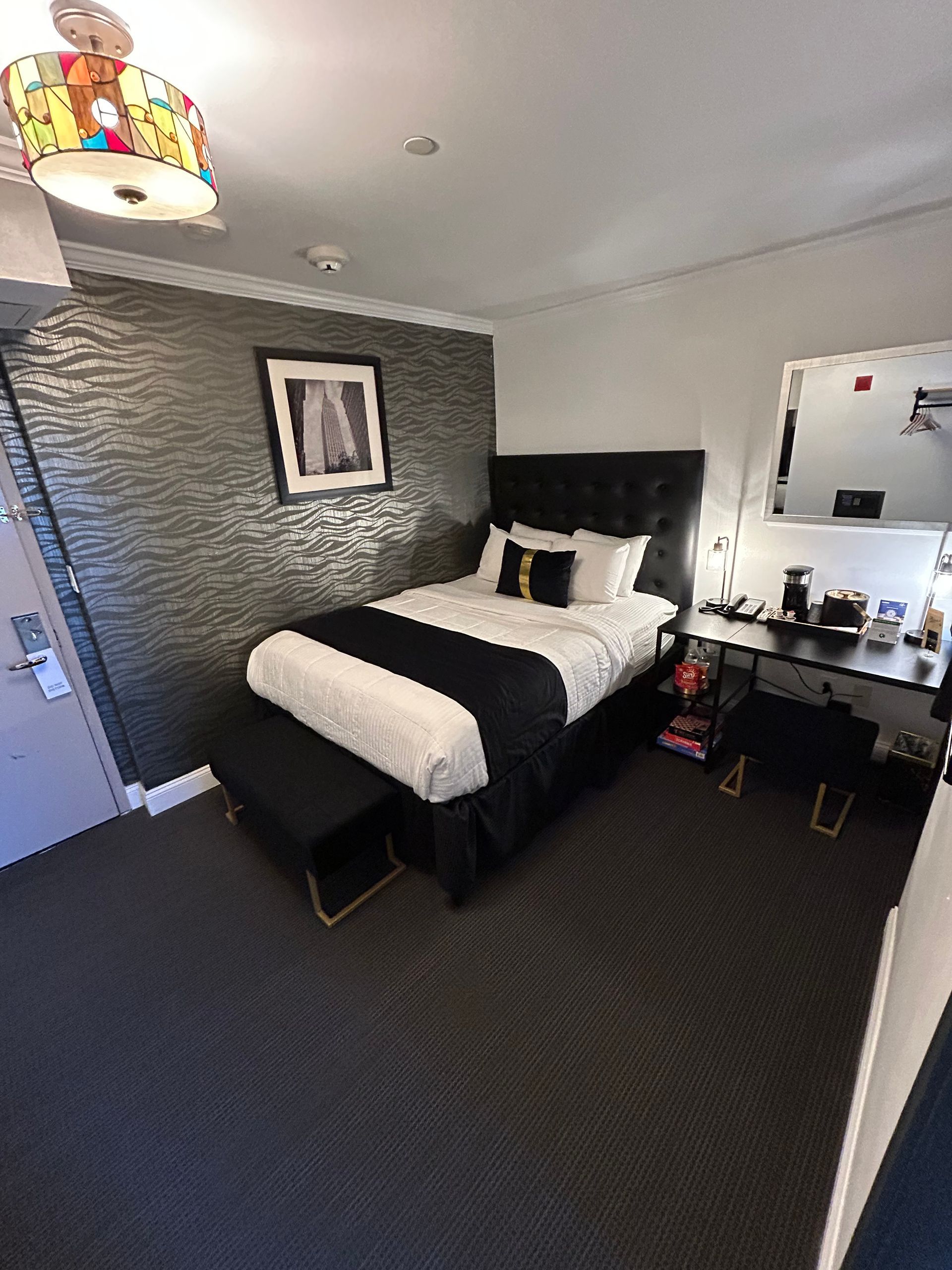 Hotel room with a single bed, black and white decor, dark gray textured wall, and desk.