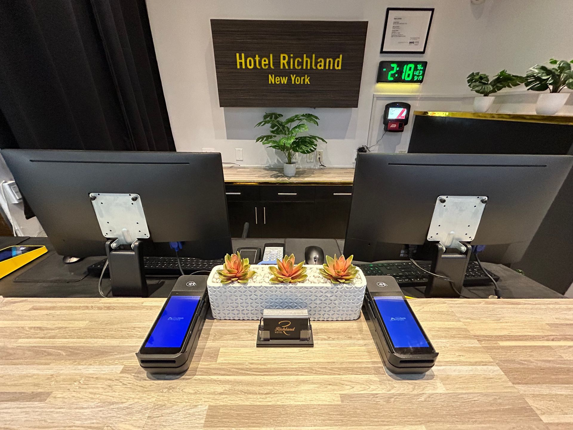 Hotel Richland reception desk with computers, payment devices, and decorative plants.