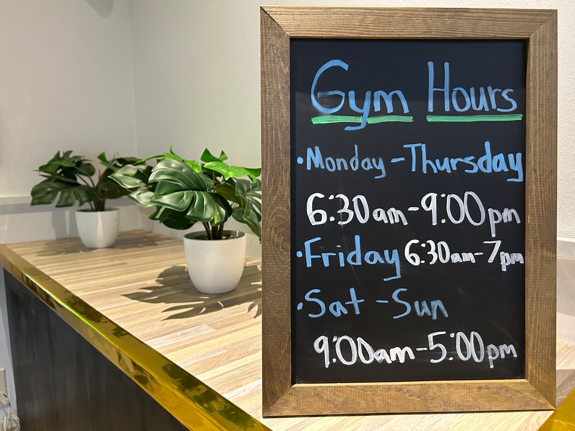 Chalkboard sign with gym hours. Monday-Thursday 6:30 am-9:00 pm. Friday 6:30 am-7 pm. Saturday-Sunday 9:00 am-5:00 pm.