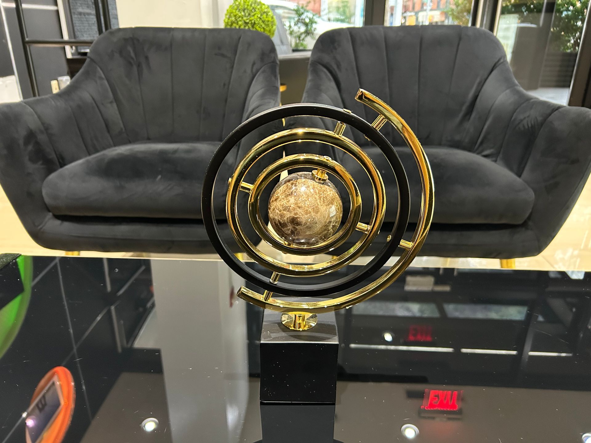 Black and gold sculpture on a glossy black table, flanked by two black velvet armchairs.