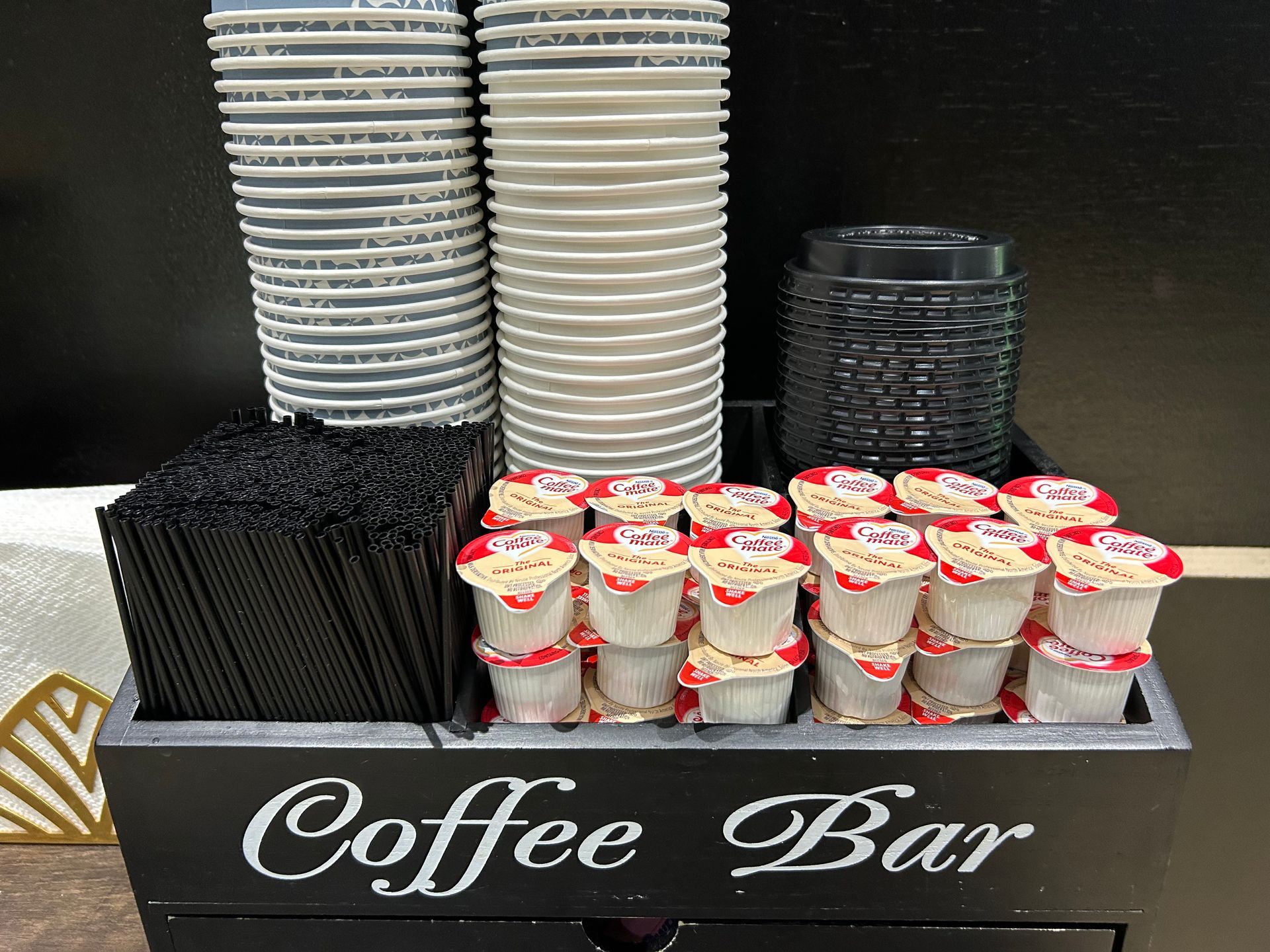 Coffee bar station with cups, stirrers, creamers, and the words 