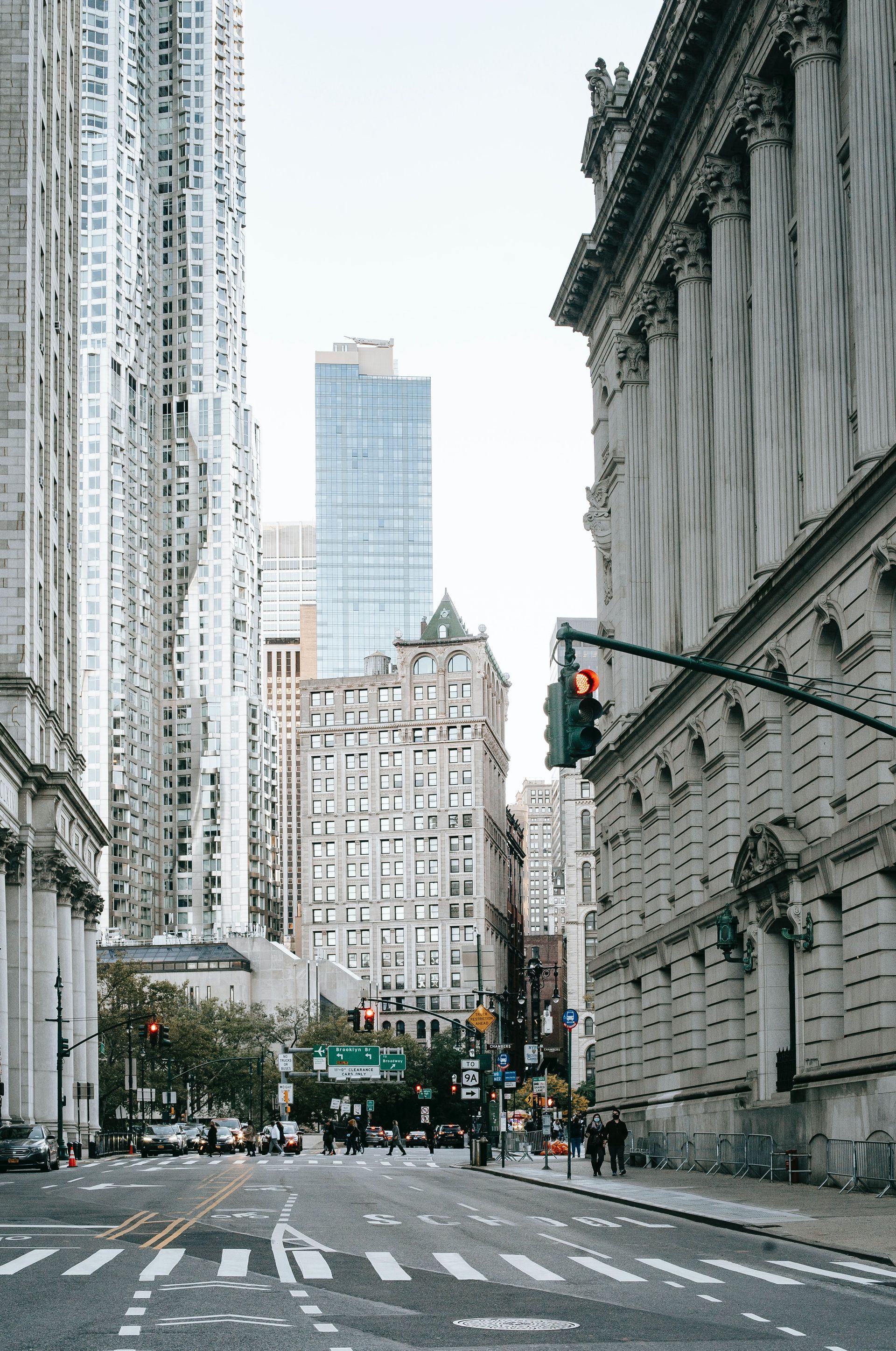 City street scene with tall buildings and traffic signal, pedestrians, and overcast sky.