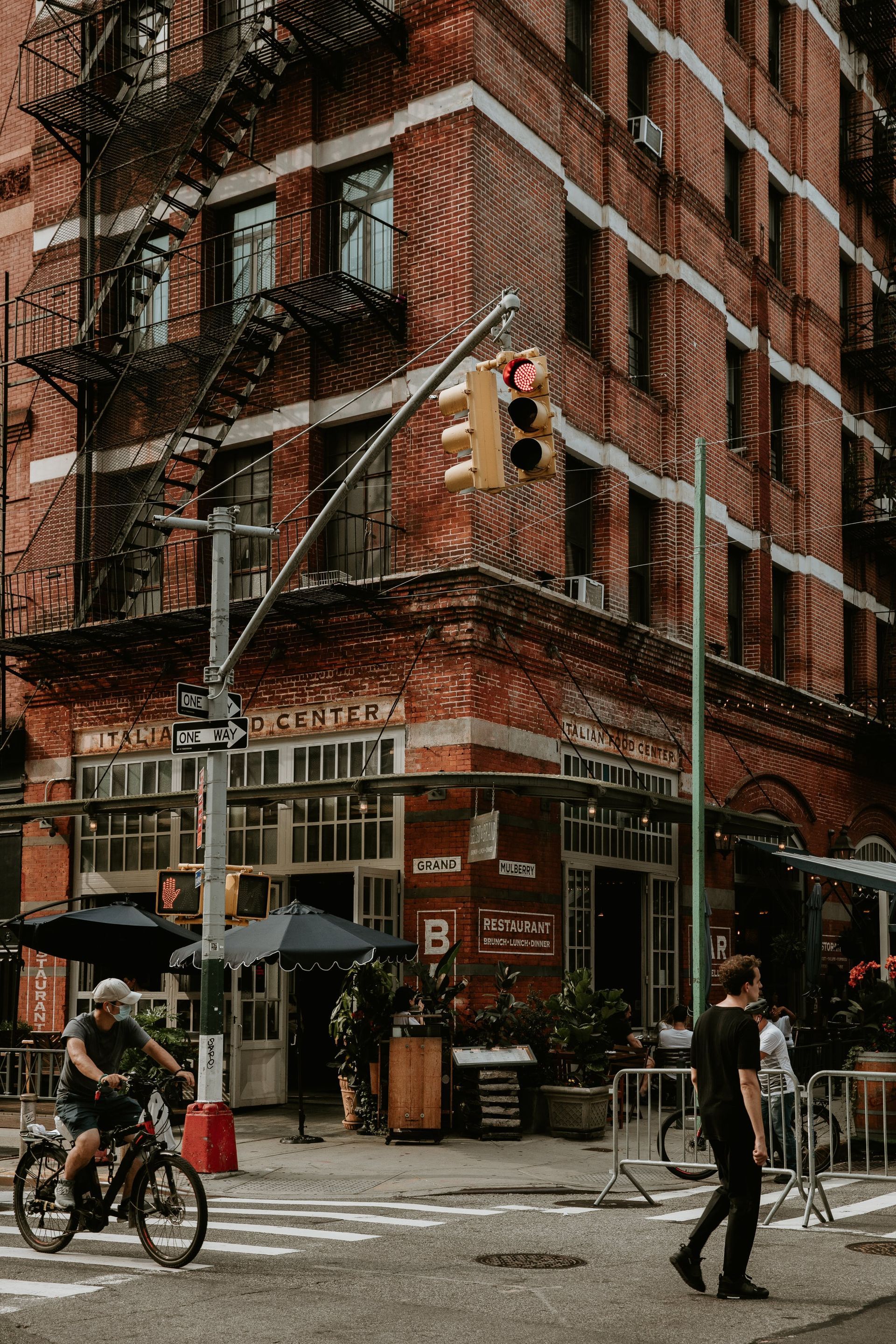 Red brick building on a city corner, people crossing street, cyclist.