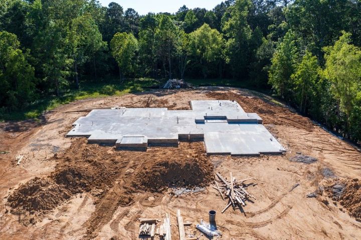 Concrete foundation of a house under construction, surrounded by dirt and trees.
