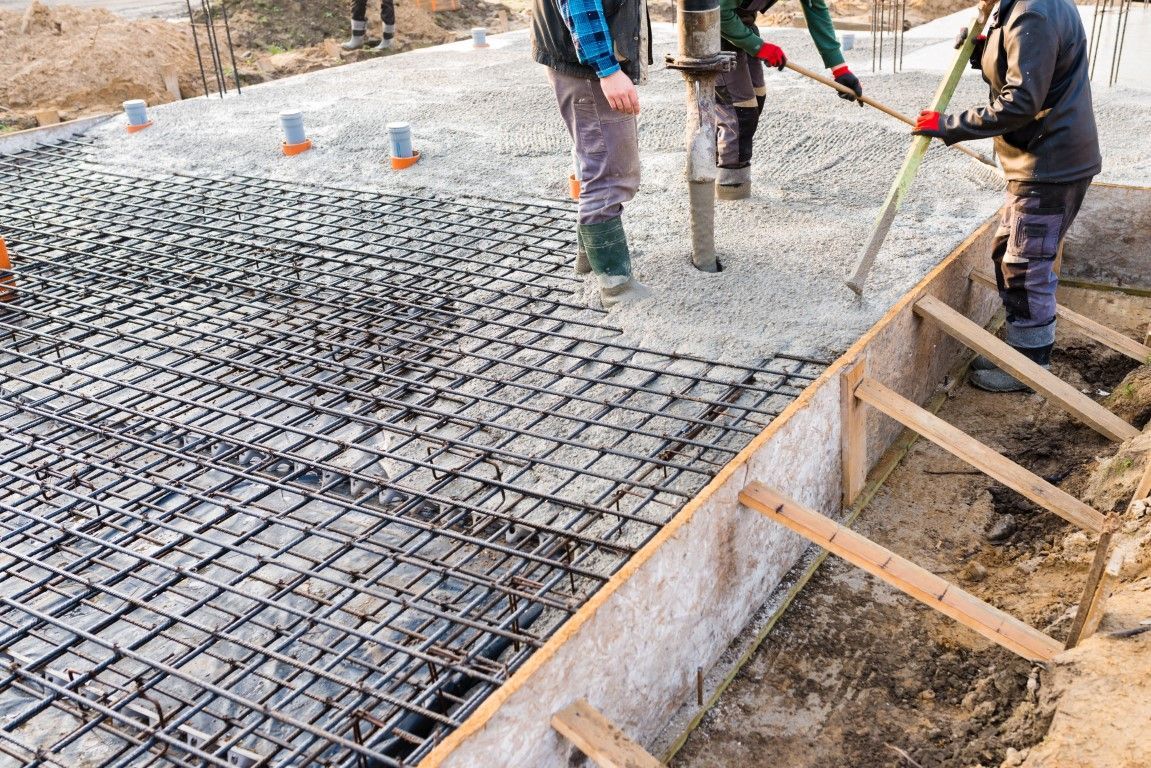 Construction workers pouring concrete onto a steel rebar grid foundation.