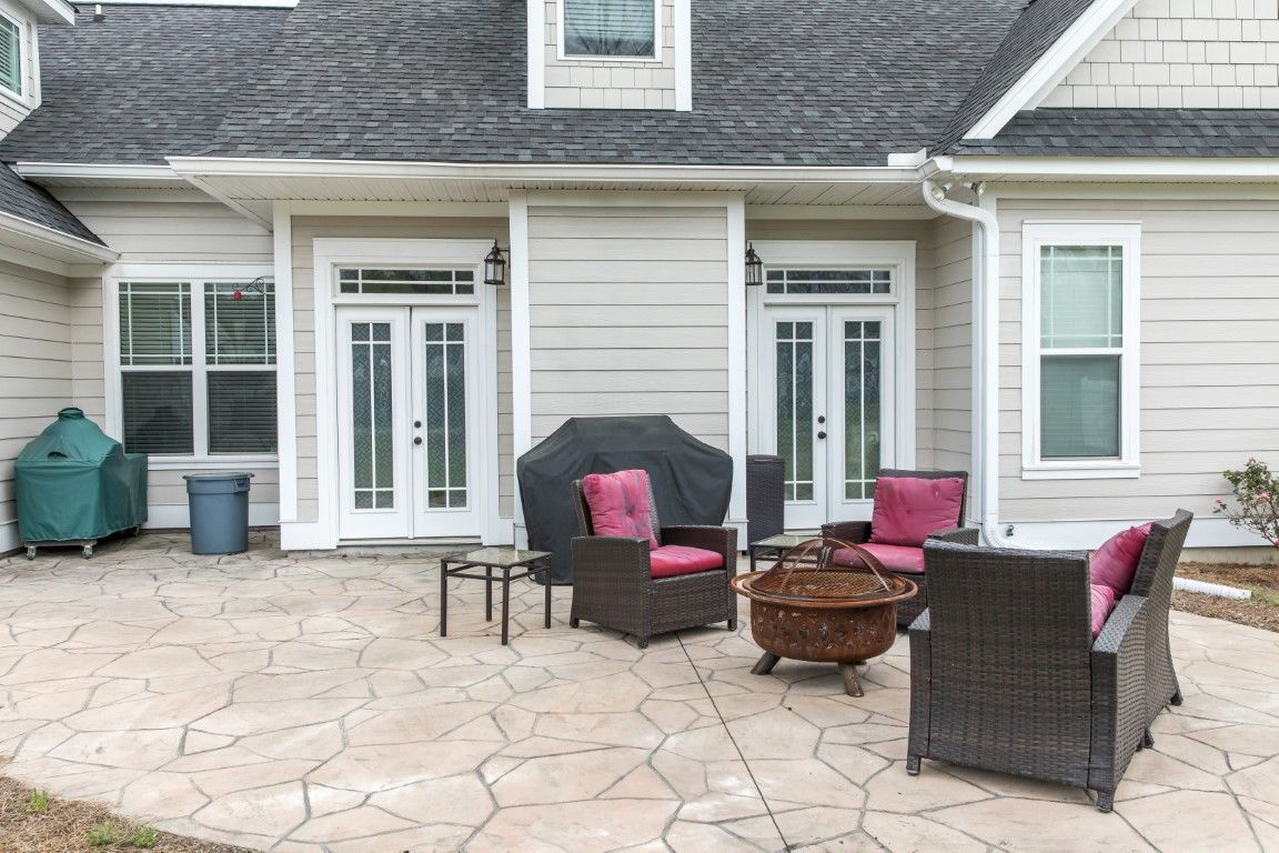 Patio with seating around a fire pit, a grill, and doors leading into a light-colored house.