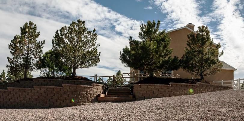 a house with a stone wall and trees in front of it