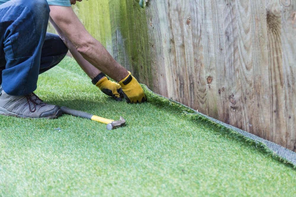 a man is installing artificial grass next to a wooden fence .